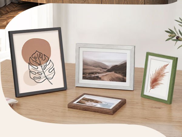 Four picture frames with different artwork and colors displayed on a wooden table.