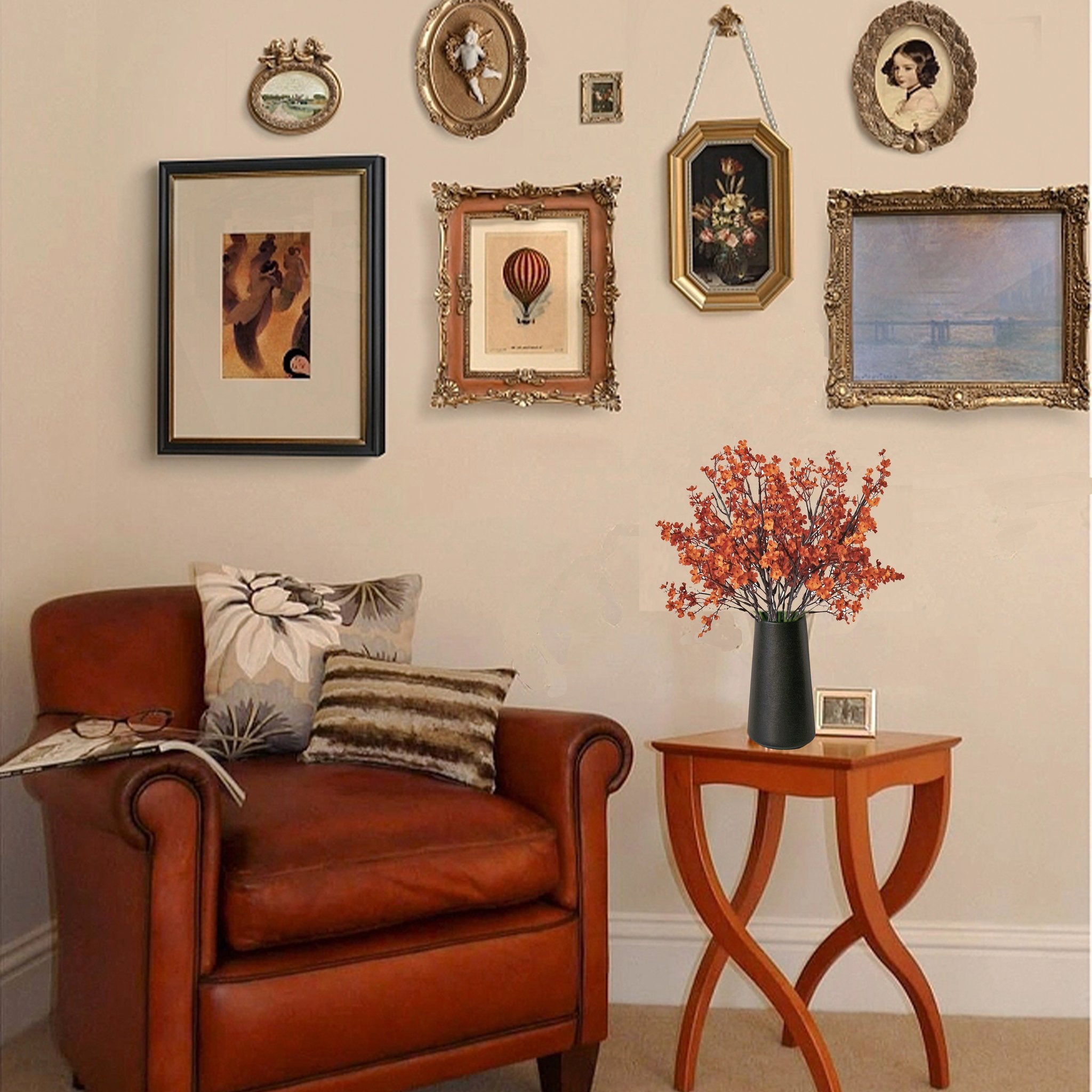 Burnt orange artificial baby's breath flowers in a black vase on a side table next to a leather armchair.