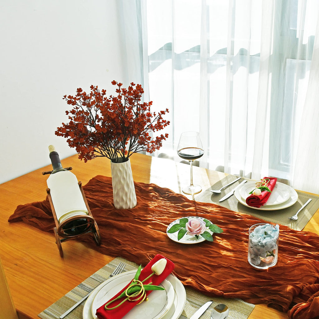 Table setting with burnt orange runner, place settings, wine bottle, and artificial floral arrangement.