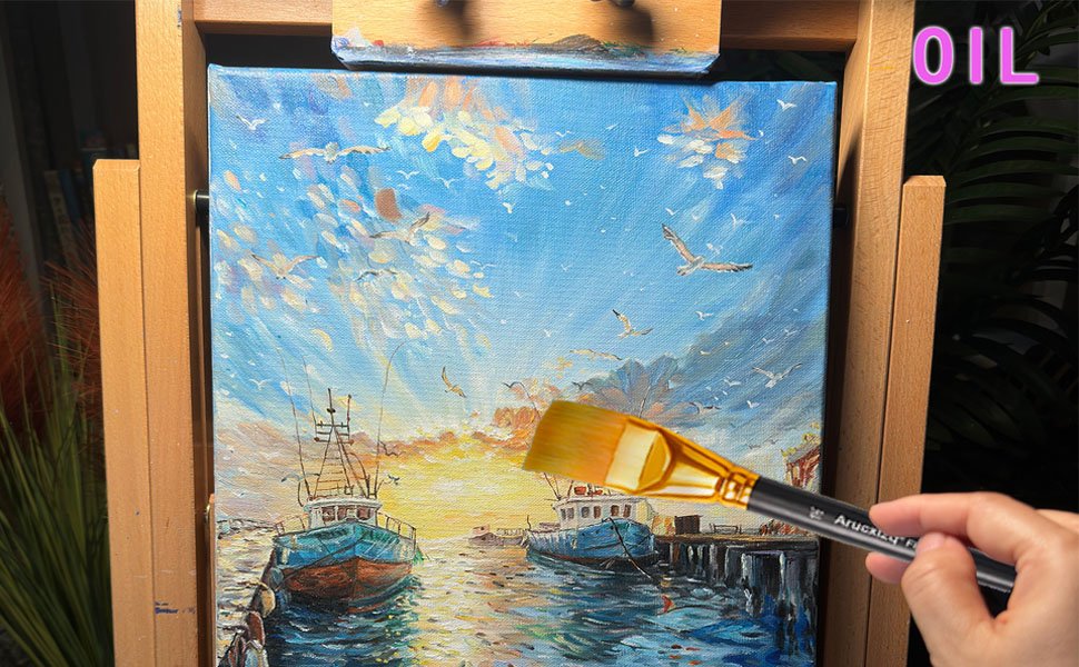 Hand holding a flat paint brush over a painting of boats at sunset, with the brush showing brand text.
