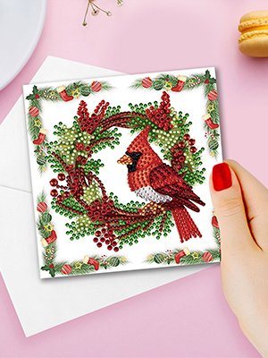 Diamond art cardinal on a Christmas wreath greeting card held by a hand with red nail polish