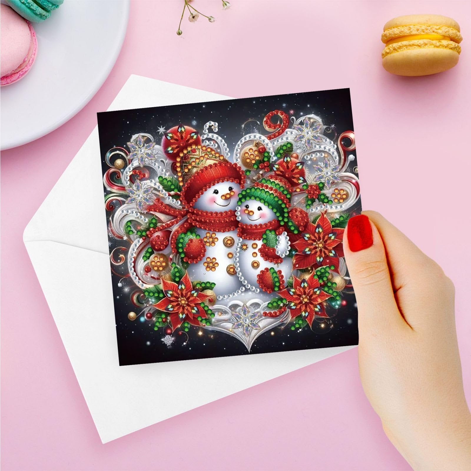 Diamond art Christmas card featuring two snowmen with festive hats and scarves, surrounded by poinsettias and snowflakes, held by a hand.