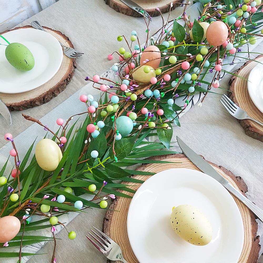 Easter egg and berry garland with green leaves draped across a table setting with wooden chargers and plates.