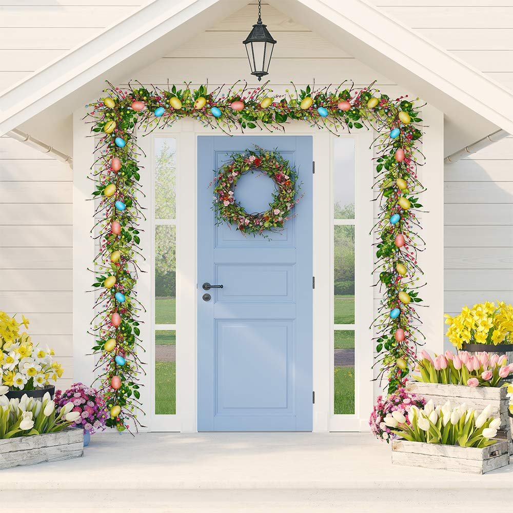 Easter garland with pastel eggs and berries draped around a blue front door, with flowers in crates.