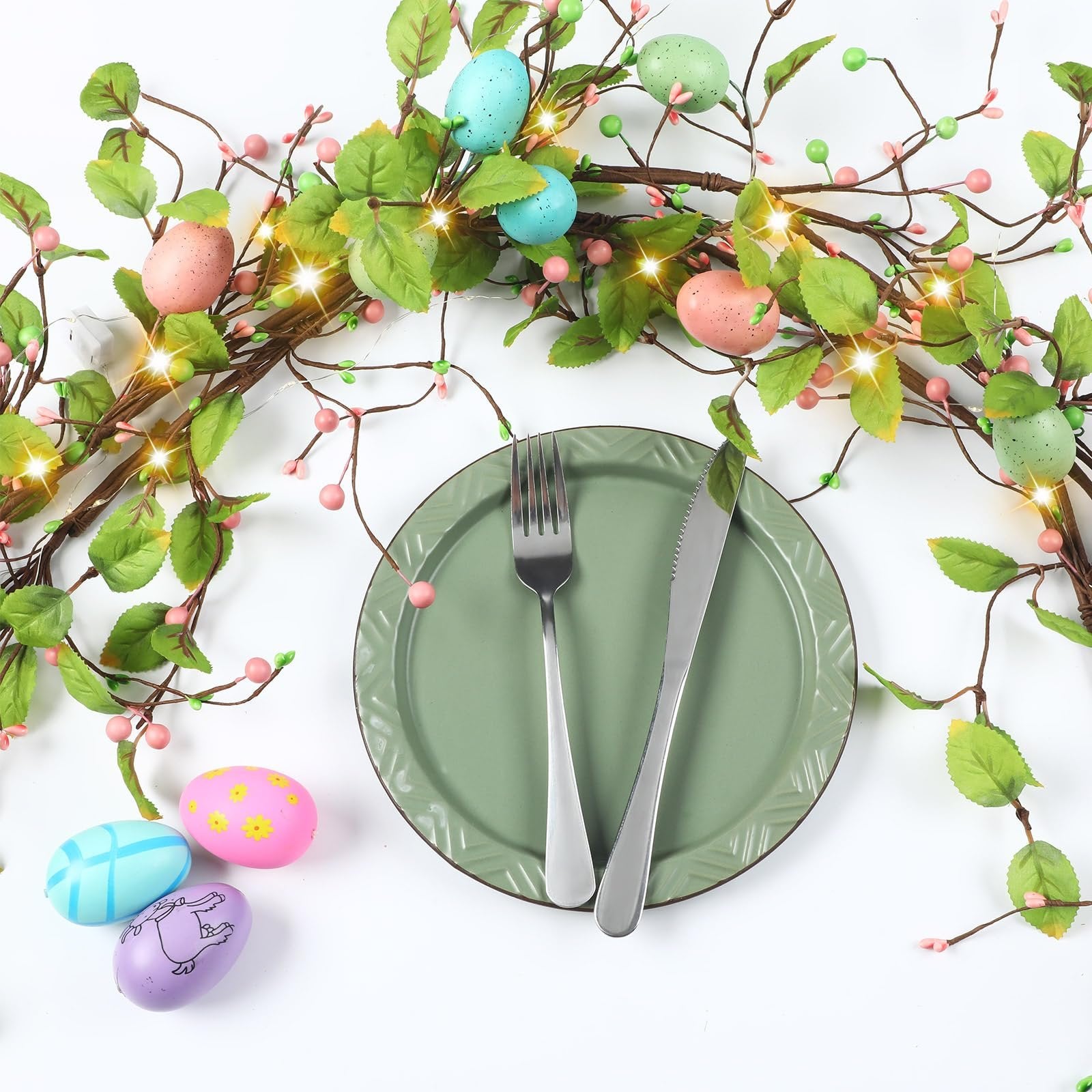 Easter egg garland with LED lights draped over a green plate with fork and knife, with loose eggs on white background