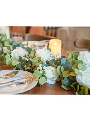 Artificial eucalyptus garland with white roses and baby's breath on a wooden table with place setting and candle