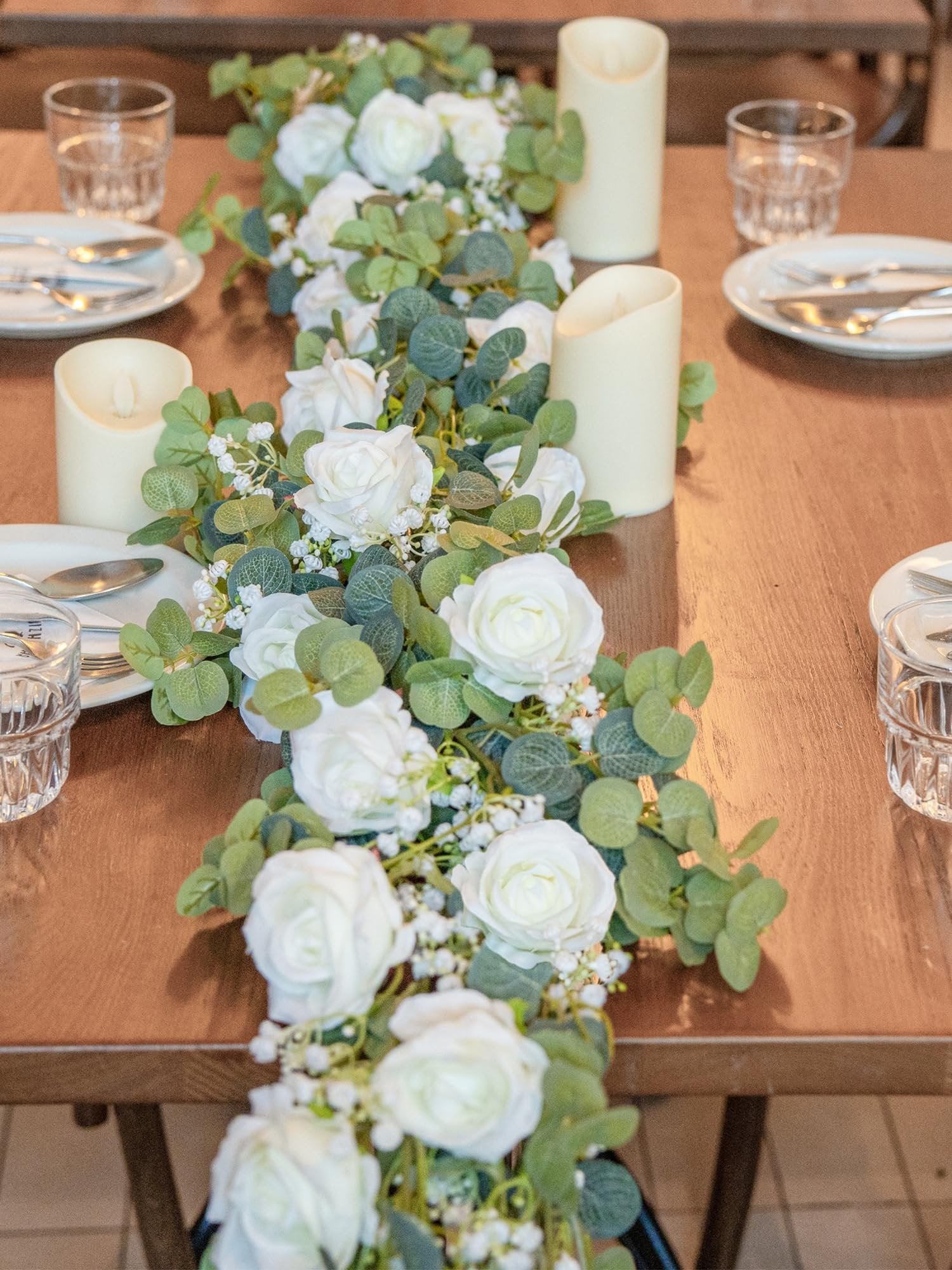 Artificial eucalyptus garland with white roses and baby's breath as a table runner with candles and place settings