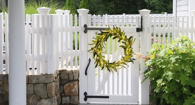Artificial olive wreath with warm white fairy lights hanging on a white picket gate