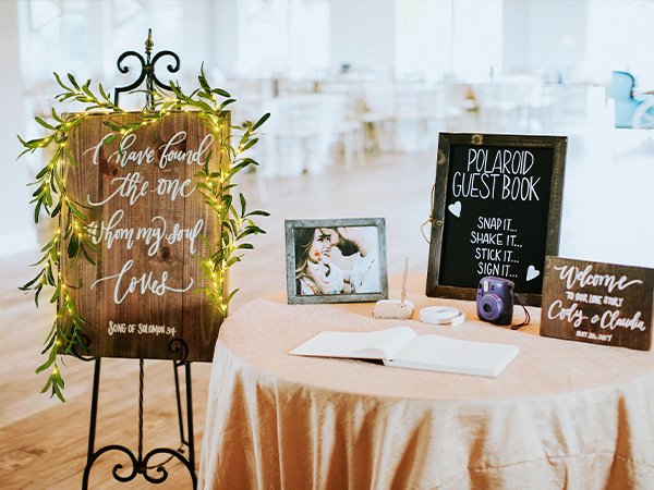 Wedding guest book table with a wooden sign featuring a quote, a Polaroid guest book station, and a welcome sign.