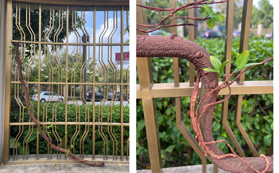 Bendable artificial tree trunk vine with leaves draped over a gold metal fence, showing close-up texture and detail.