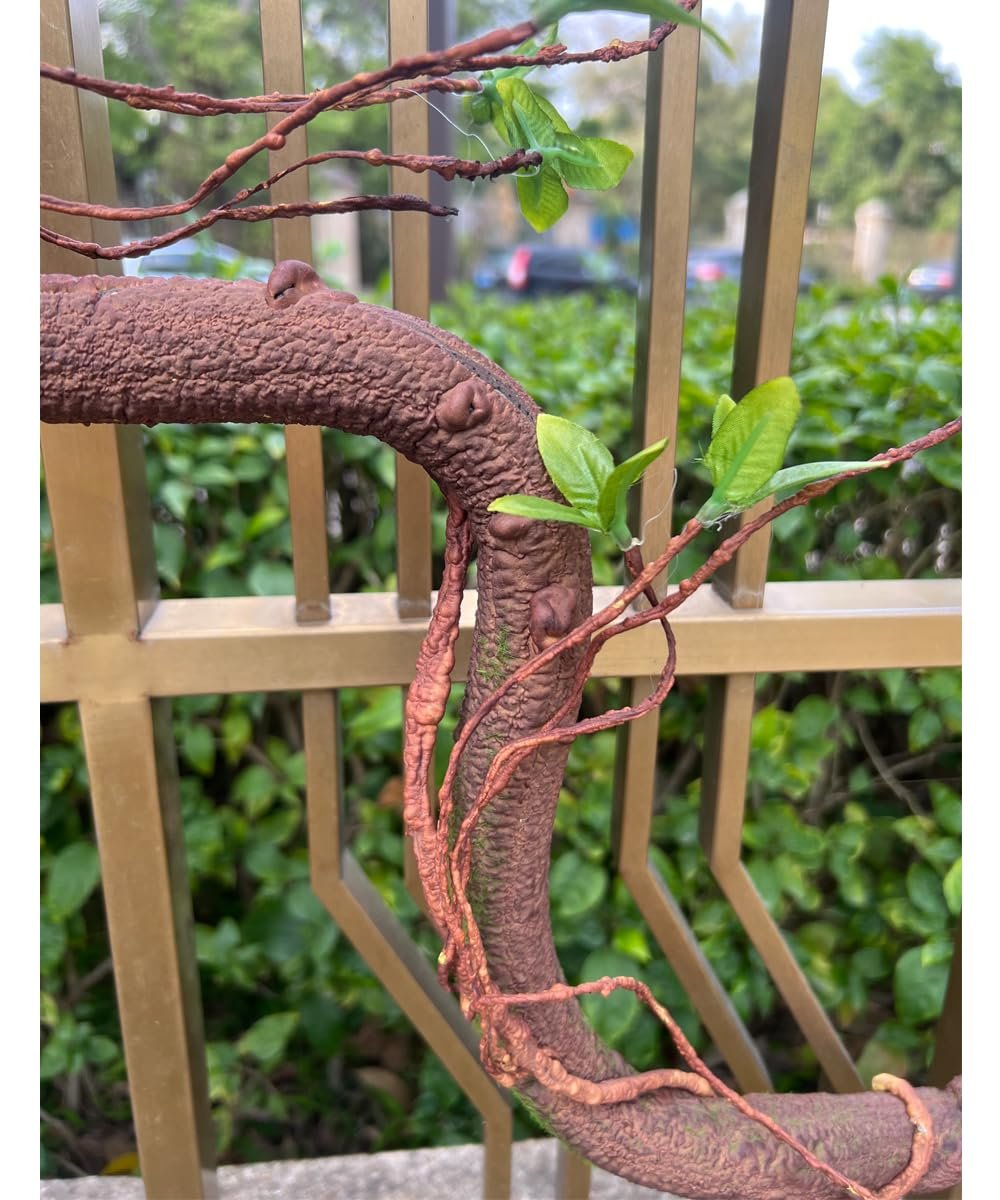 Close-up of a bendable artificial tree trunk vine with faux moss and green leaves, draped over a golden railing.