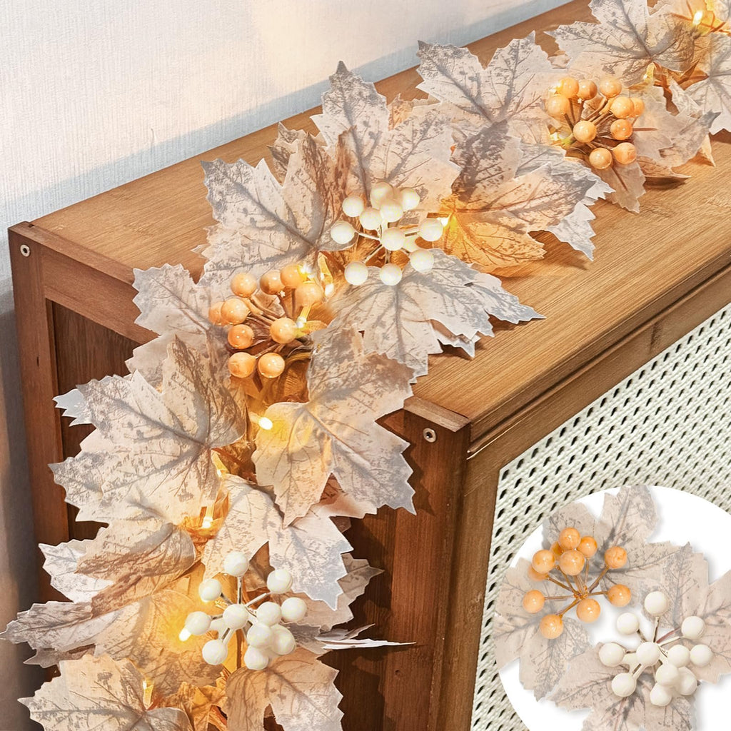 Fall garland with silk maple leaves, berries, and warm white LED lights draped on a wooden surface.