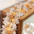 Fall garland with silk maple leaves, berries, and warm white LED lights draped on a wooden surface.