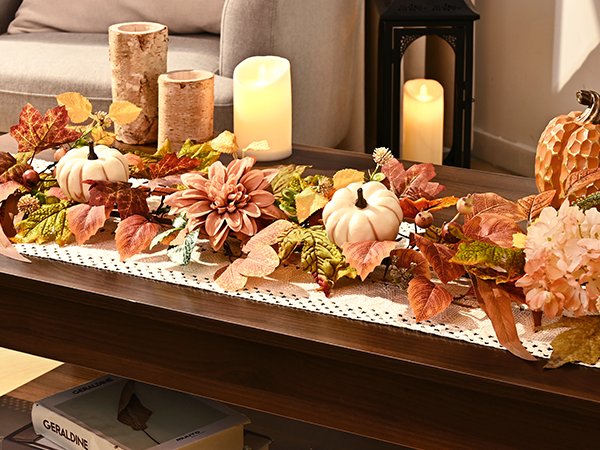 Fall garland with artificial leaves, pumpkins, and flowers arranged on a table runner with decorative candles and a lantern.