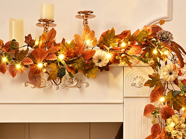 Autumn garland with artificial leaves, pumpkins, berries, and lights draped over a white mantlepiece with candles.