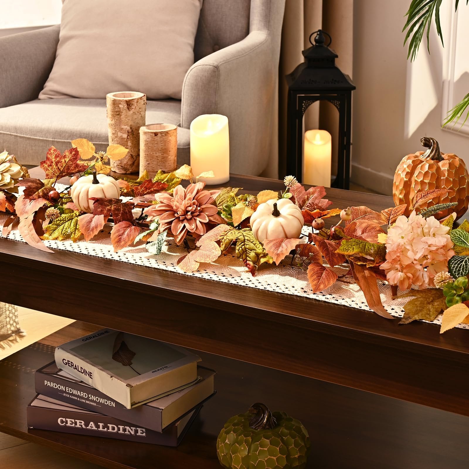 Fall garland with artificial leaves, pumpkins, and flowers arranged on a table with candles and a lantern.