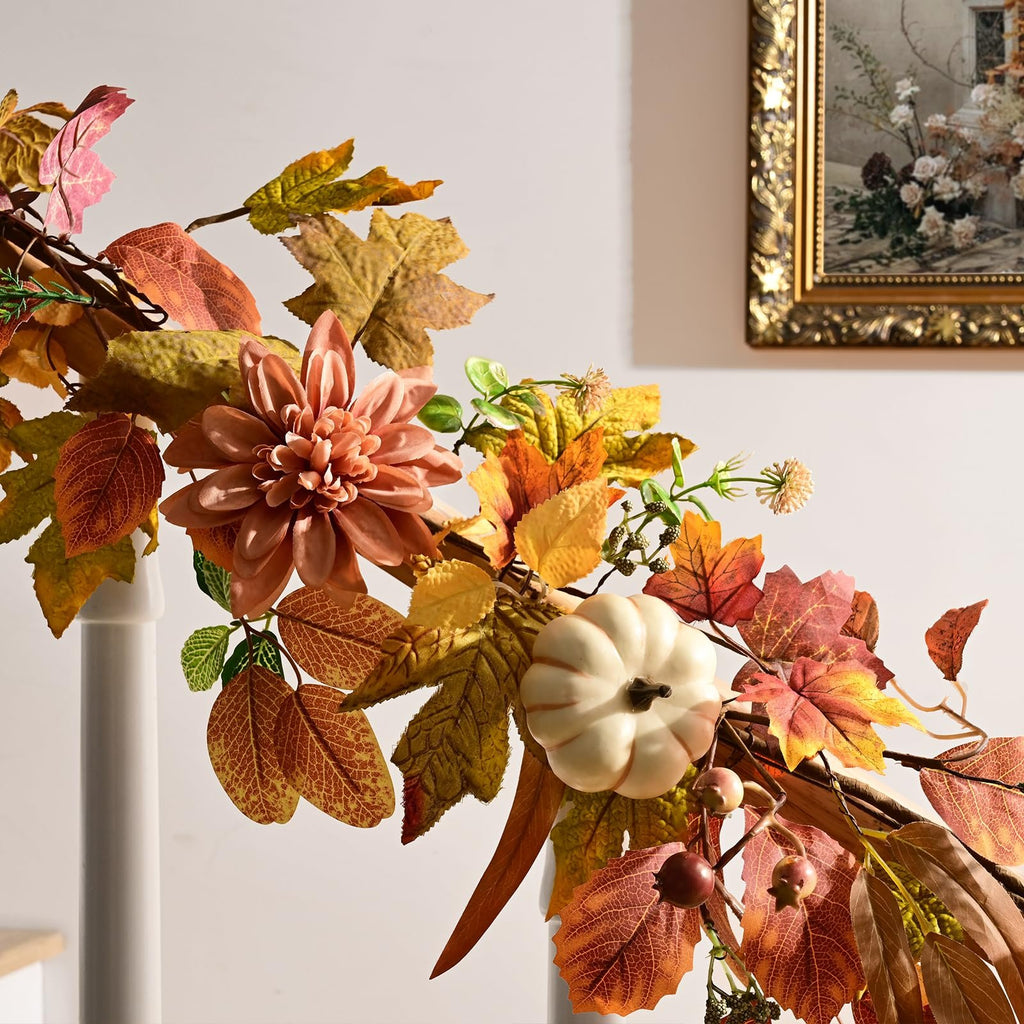 Autumn garland with artificial leaves, a white pumpkin, and a peach-colored flower, displayed against a wall with a framed painting.