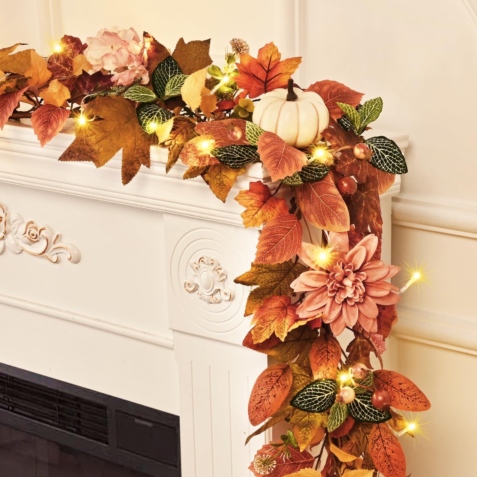 Autumn garland with lights, leaves, pumpkins, and flowers draped over a white mantlepiece.
