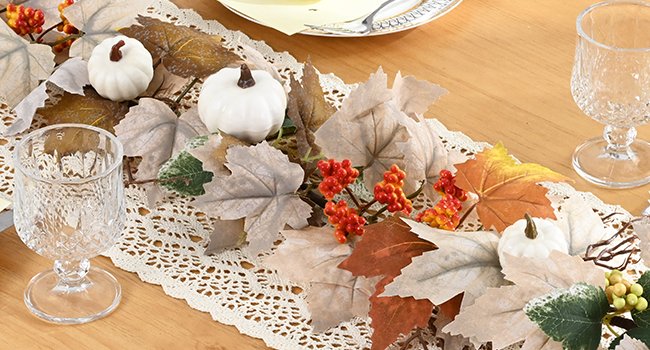 Fall garland with artificial maple leaves, white pumpkins, and red berries on a lace table runner.