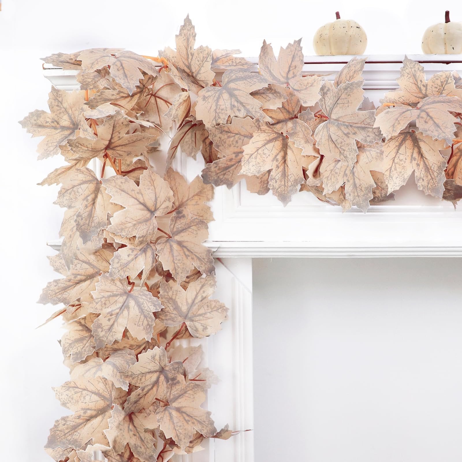 Autumn maple leaf garland draped over a white mantle with two decorative pumpkins on top.