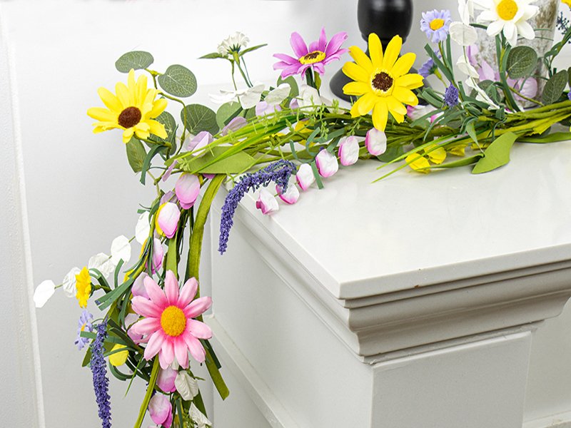Farmhouse spring flower garland with pink daisies, yellow sunflowers, and lavender on a white surface.