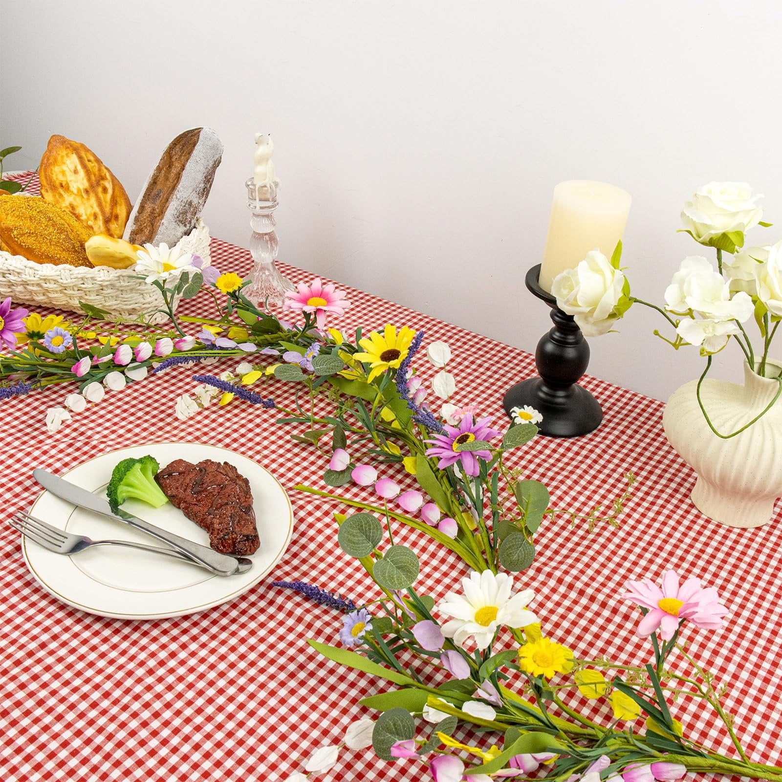 Farmhouse spring flower garland with pink, white, yellow wildflowers and daisy accents draped across a table setting with bread, steak, and candles.