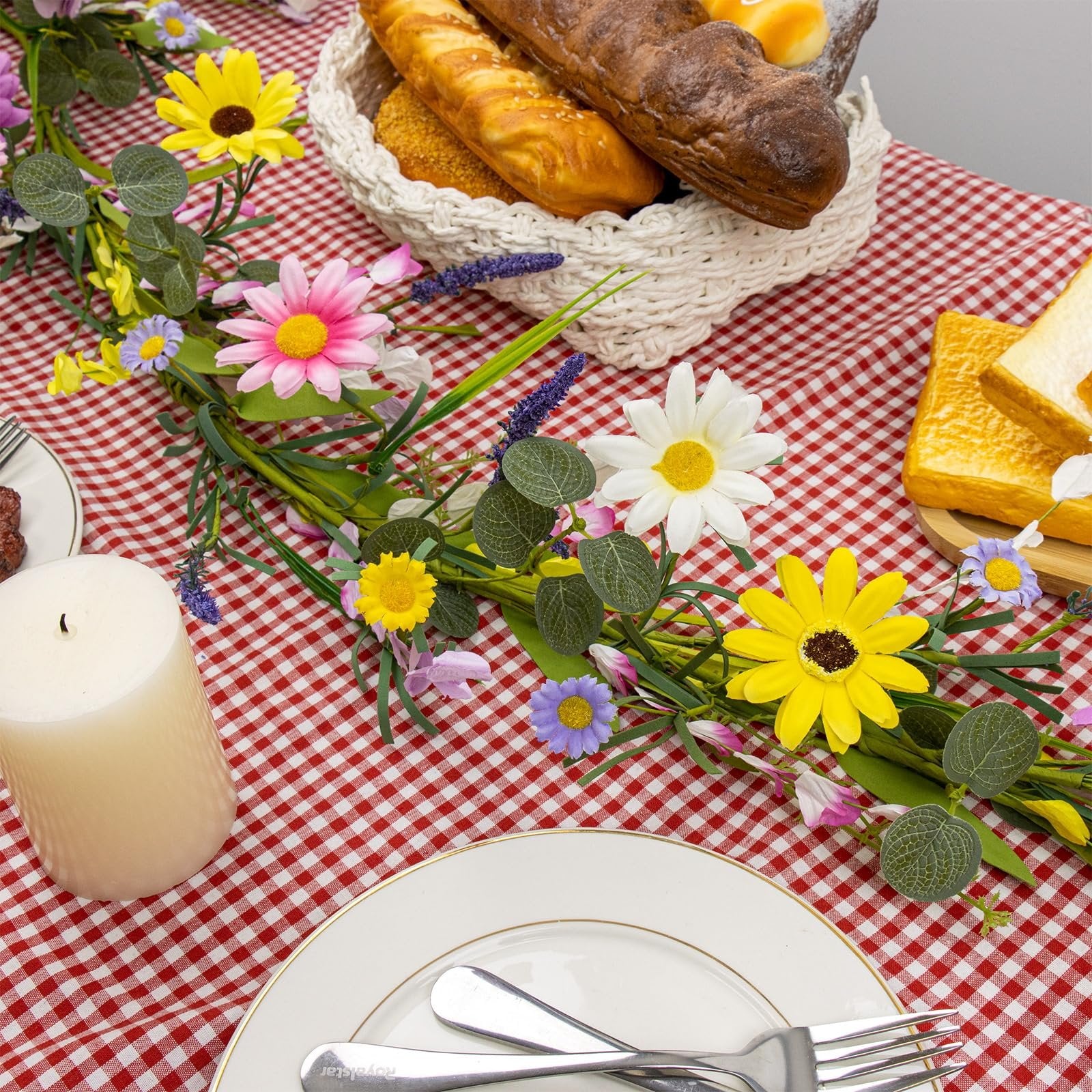 Farmhouse spring flower garland with pink, white, and yellow wildflowers arranged on a red and white checkered tablecloth with bread and toast.