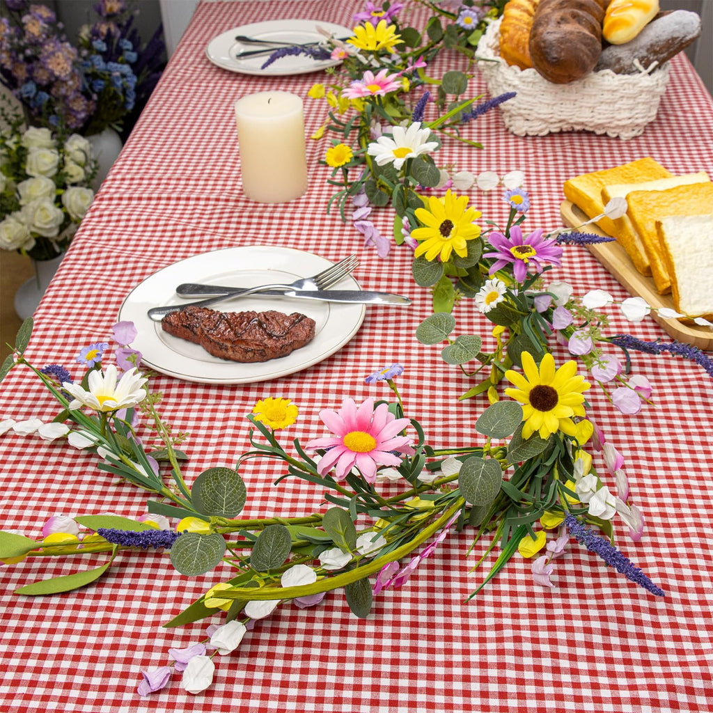 Farmhouse spring flower garland with pink, white, yellow wildflowers and daisies draped on a red and white checkered tablecloth.