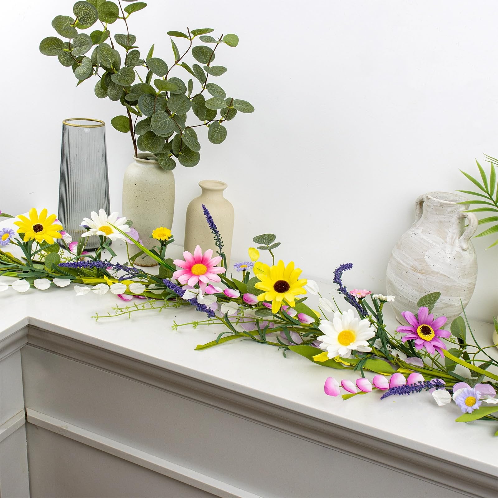 Farmhouse spring flower garland with pink, yellow, and white daisies and lavender accents on a white surface.