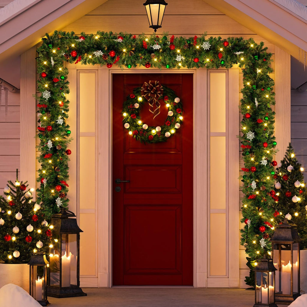 Christmas garland and wreath adorn a red front door with two small decorated trees and lanterns on the porch.