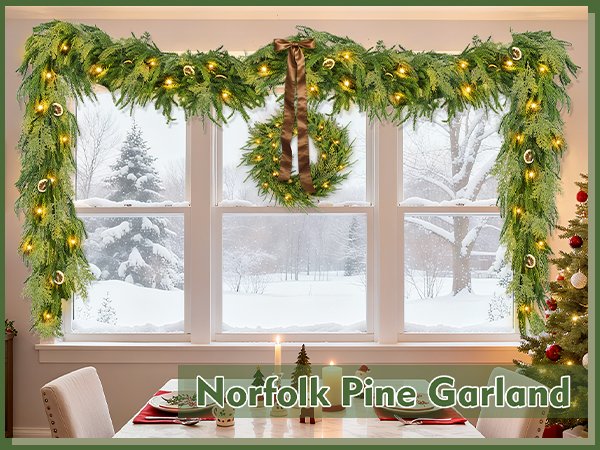 Prelit Christmas garland with lights and pinecones draped across a window with a snowy scene outside.