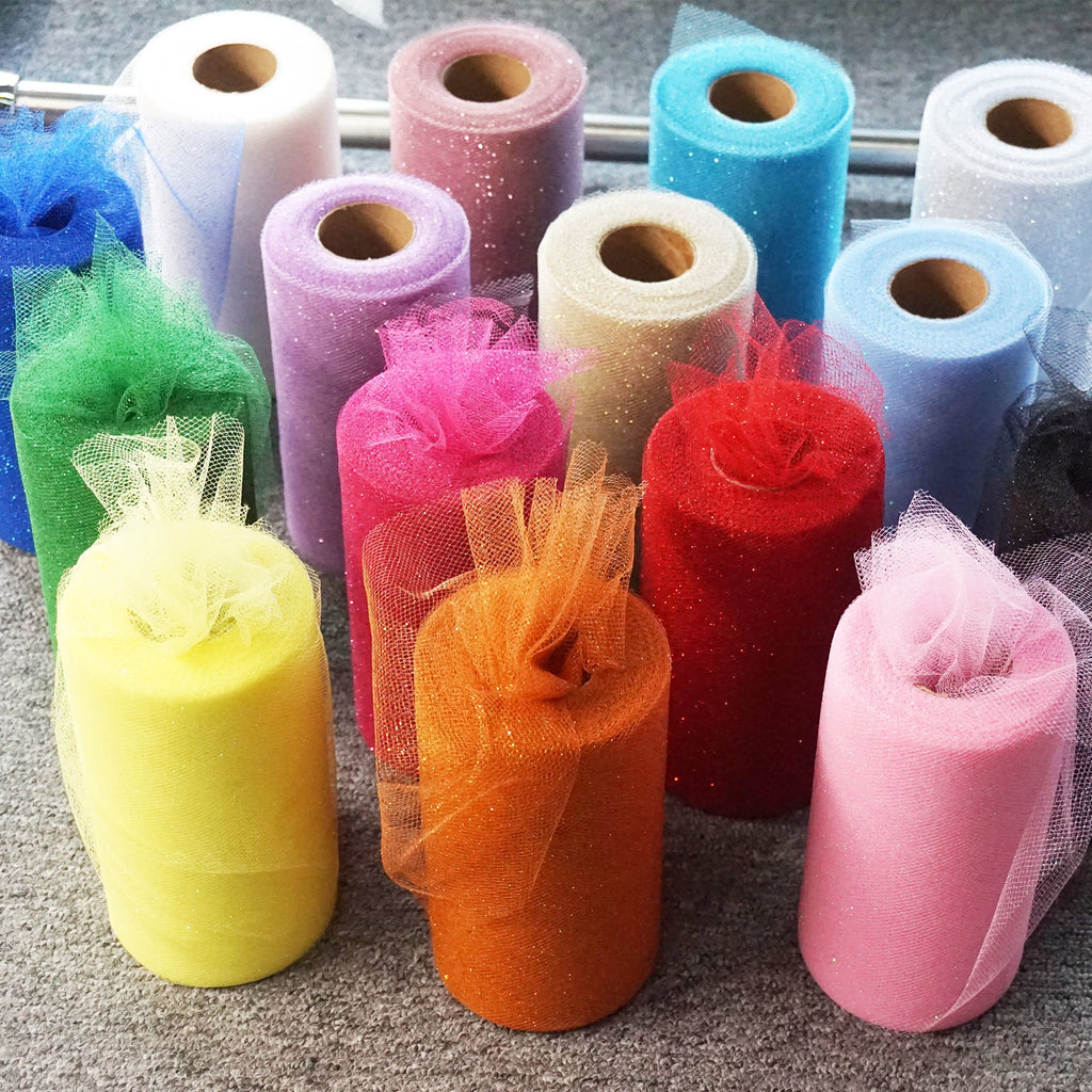 Assortment of glitter tulle fabric rolls in various colors including yellow, orange, pink, red, purple, blue, and white, arranged on a gray surface.