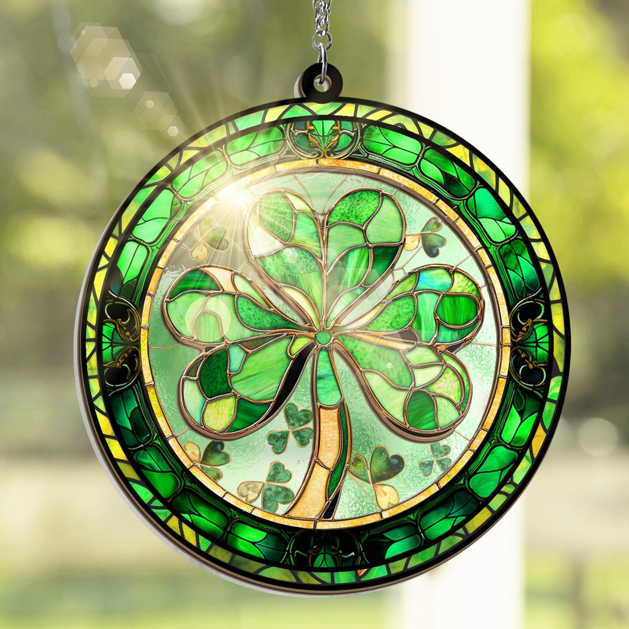 Round stained glass suncatcher with a shamrock design, hanging by a chain against a blurred green background.