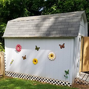 Metal sunflower and butterfly wall art decor pieces attached to the side of a white shed.