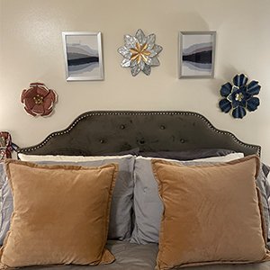 Metal wall art decor including sunflowers and abstract paintings arranged above a bed with pillows.