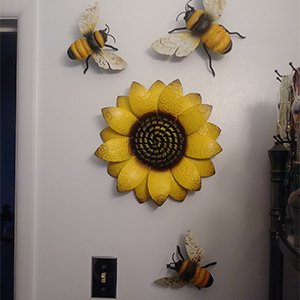 Metal sunflower wall art with three bees arranged on a white wall near a light switch.