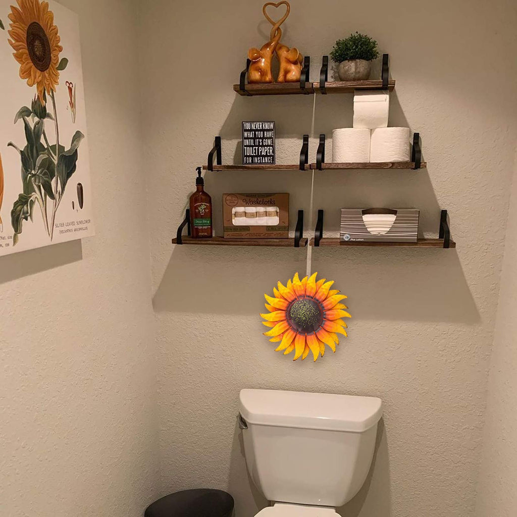 Metal sunflower wall art decor hanging above a toilet, with shelves holding toiletries and a sunflower print on the left.