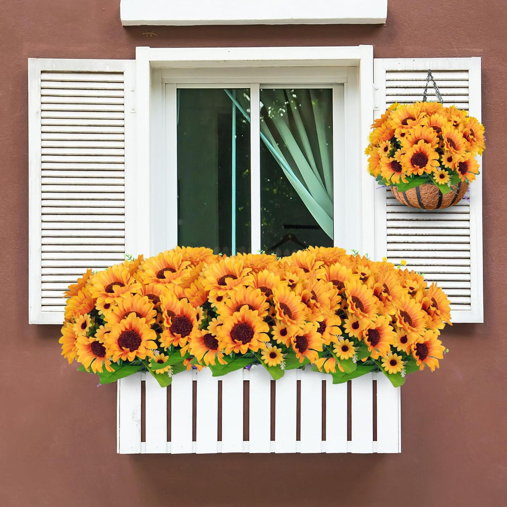 Artificial sunflowers in a white window box and a hanging basket on a brown wall with white shutters.