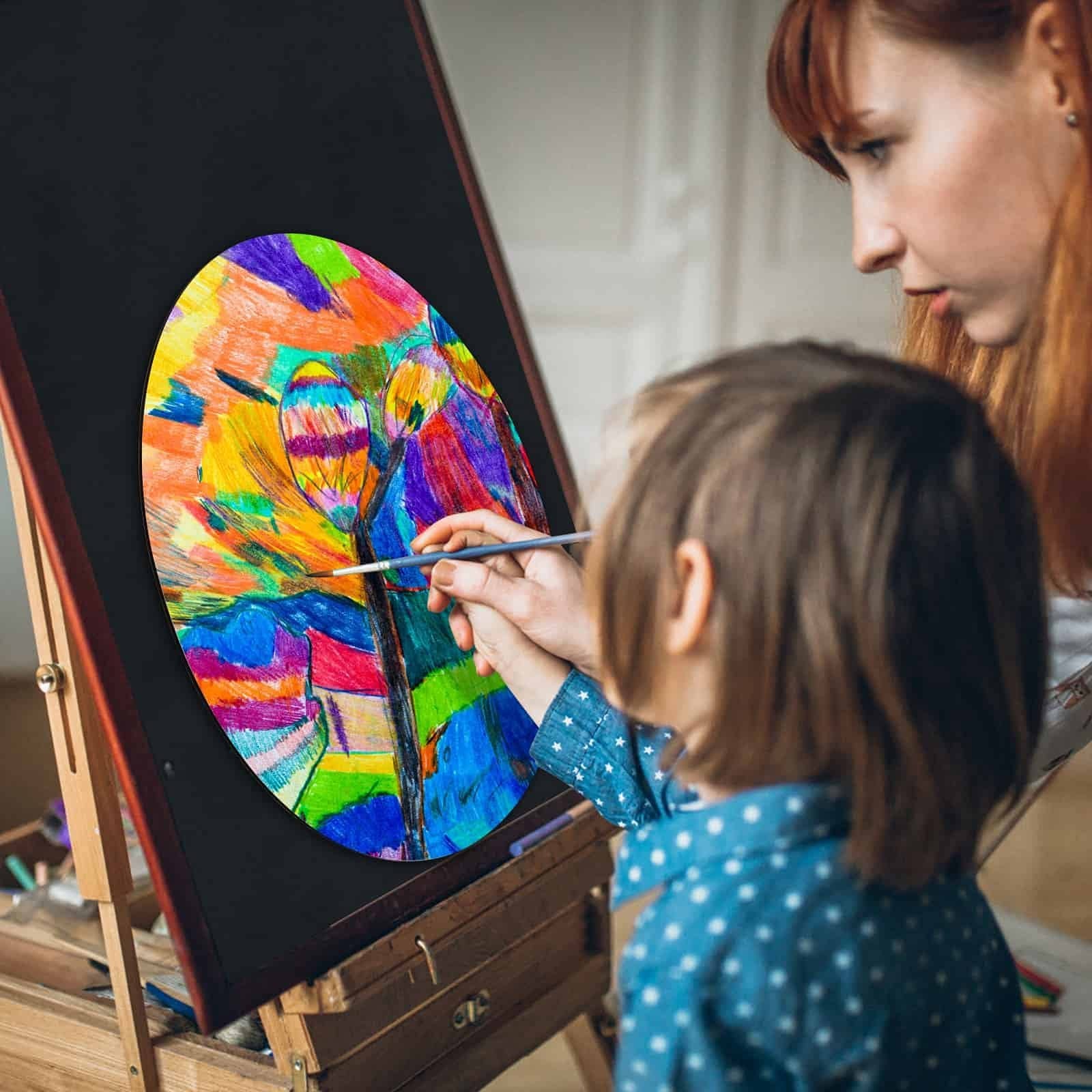 Woman and child painting on a large wooden circle displayed on an easel