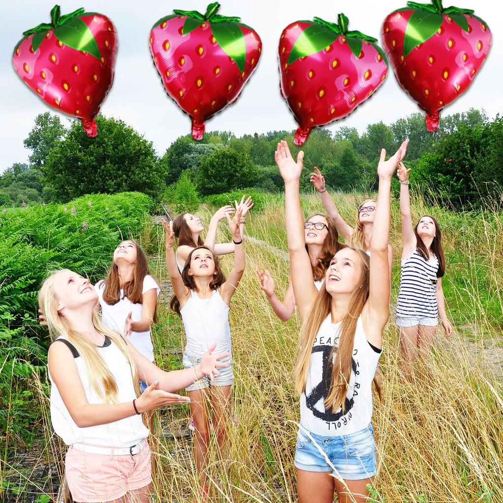Group of girls reaching for strawberry-shaped balloons in a grassy field