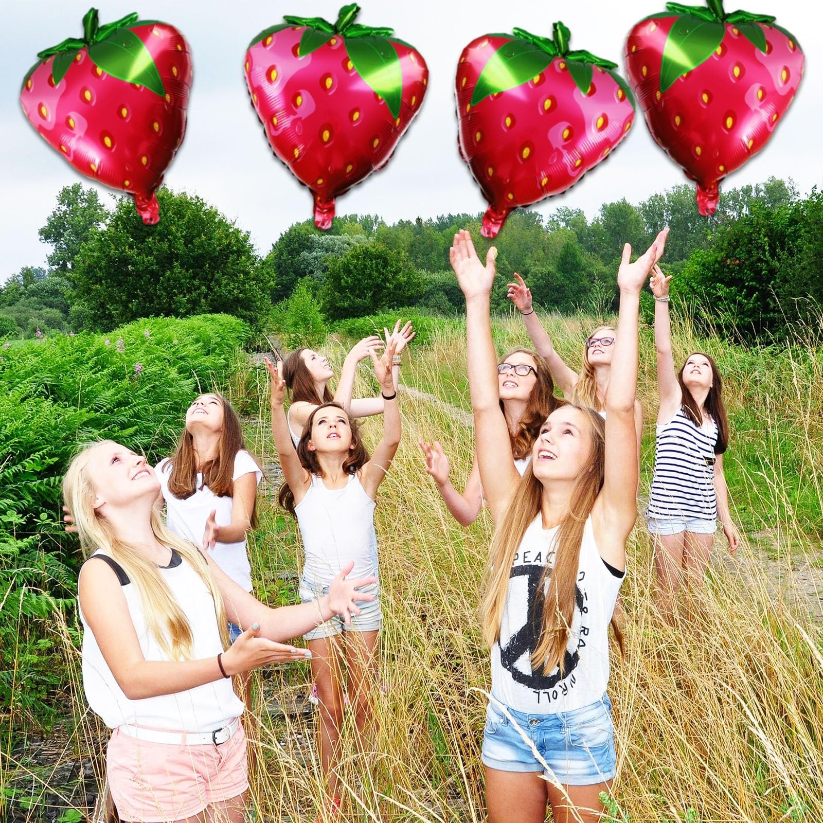 Group of girls reaching for strawberry-shaped balloons in a grassy field