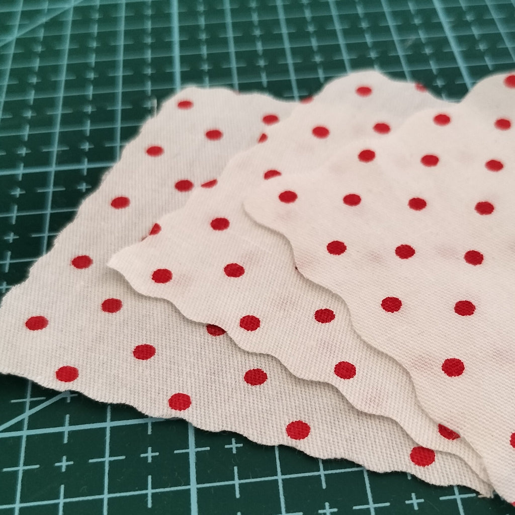 Three swatches of white fabric with red polka dots layered on a green cutting mat.