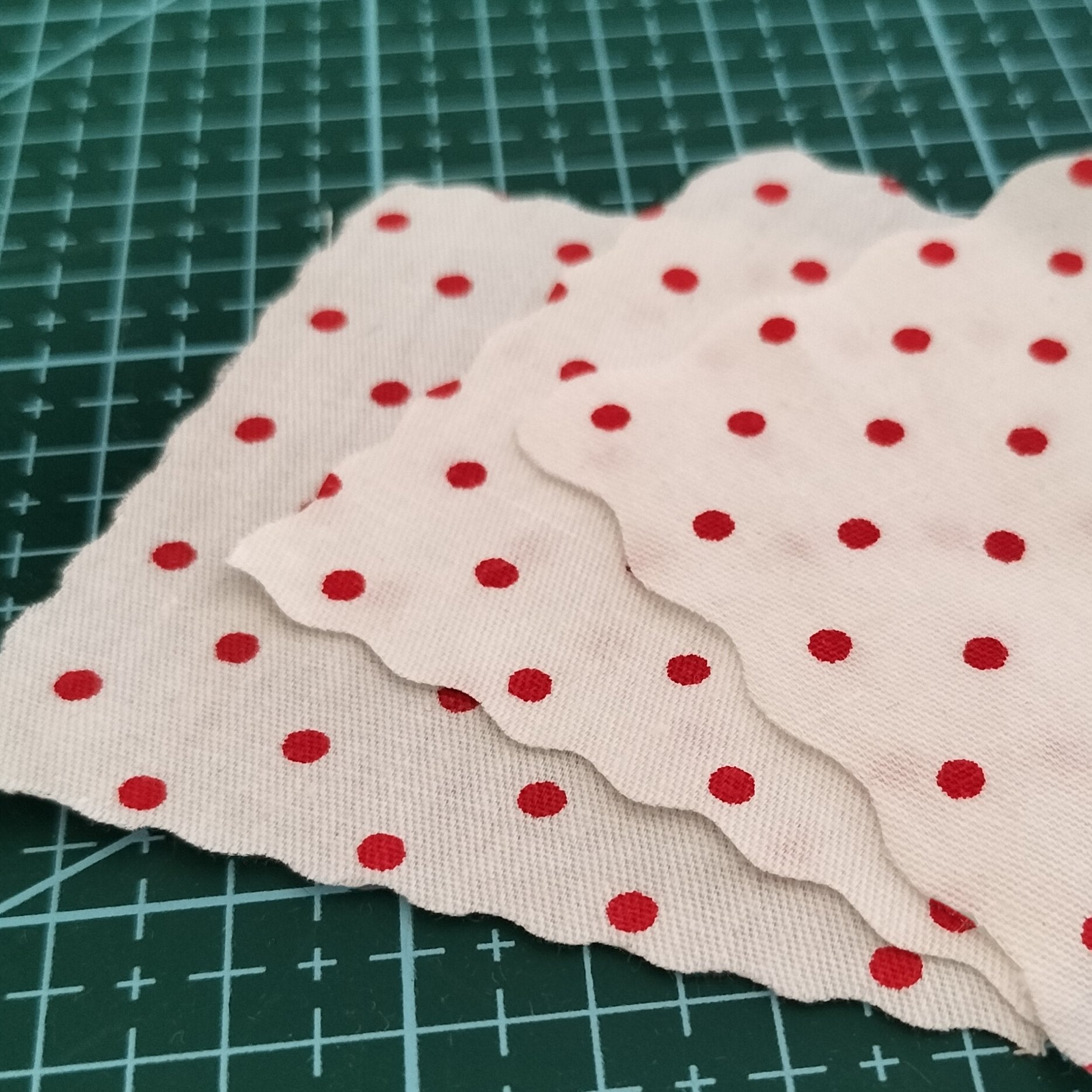 Three swatches of white fabric with red polka dots layered on a green cutting mat.
