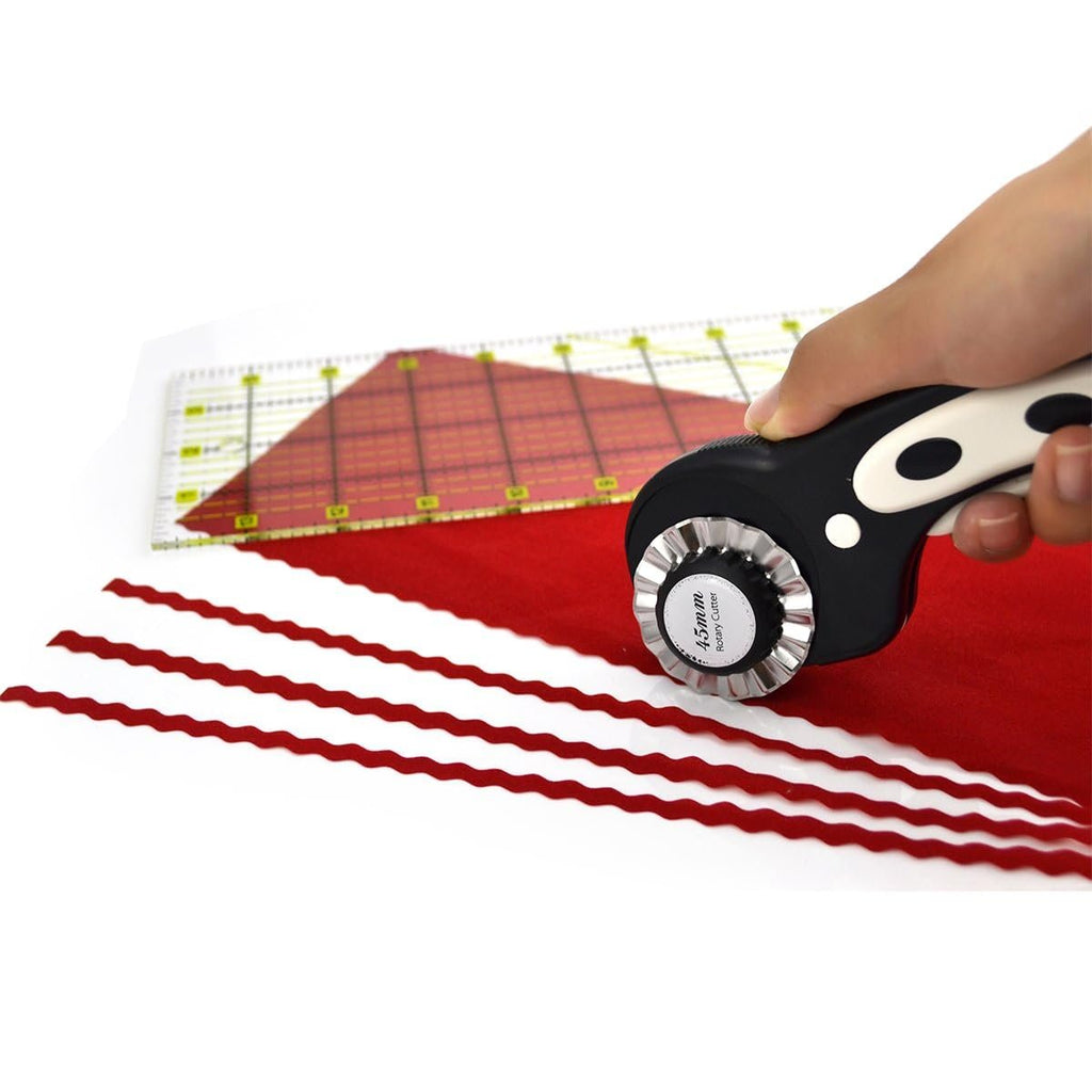 Hand holding a pinking rotary cutter cutting red fabric with a quilting ruler in the background