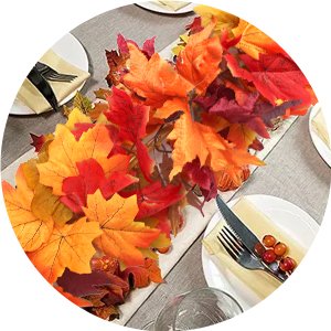 Artificial fall maple leaf garland with red, orange, and yellow leaves draped on a table runner with place settings.