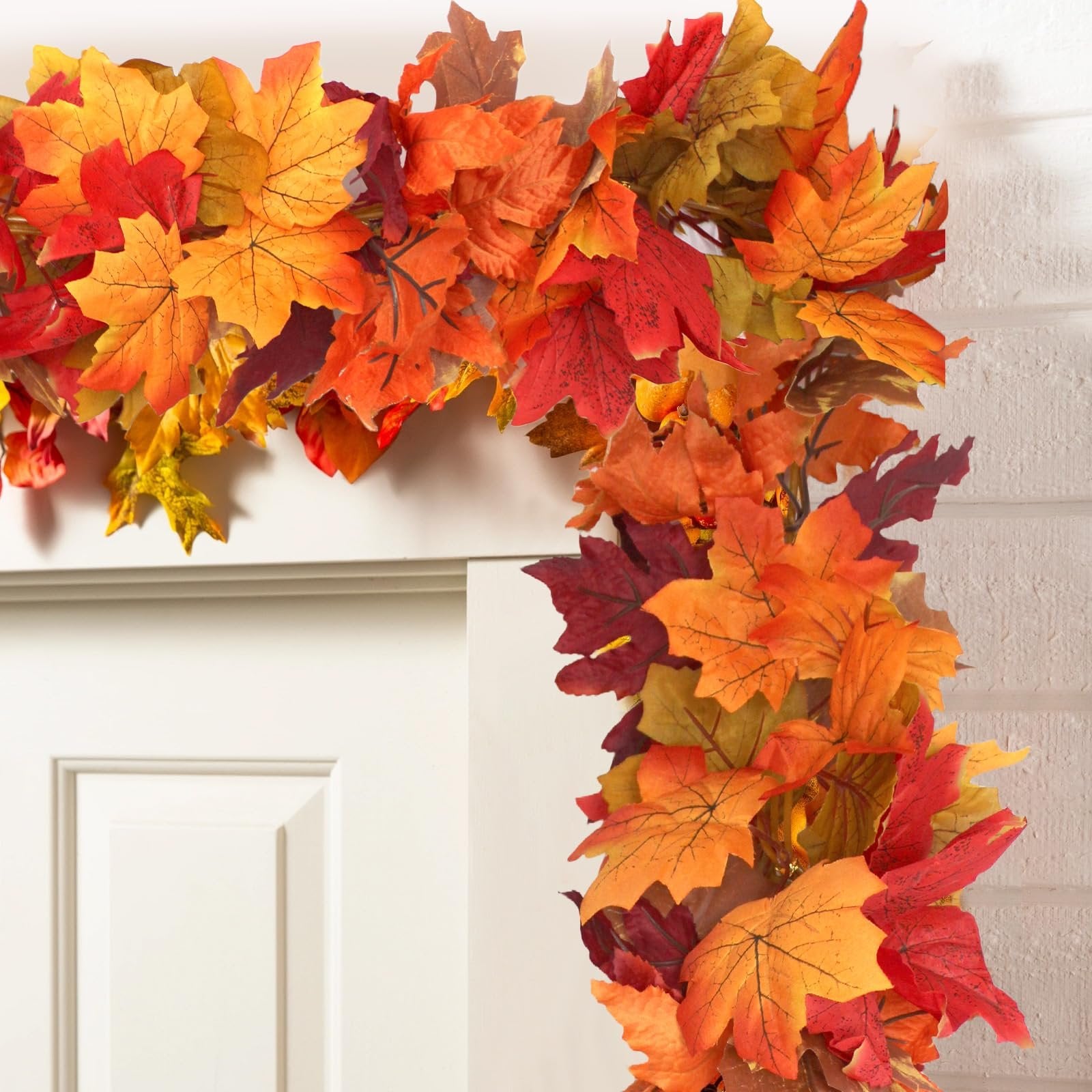 Artificial fall maple leaf garland draped over a white door frame, featuring vibrant red, orange, and yellow leaves.