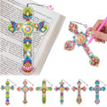 Diamond art cross bookmarks with rhinestones displayed on an open book and a hand holding a pink tool.