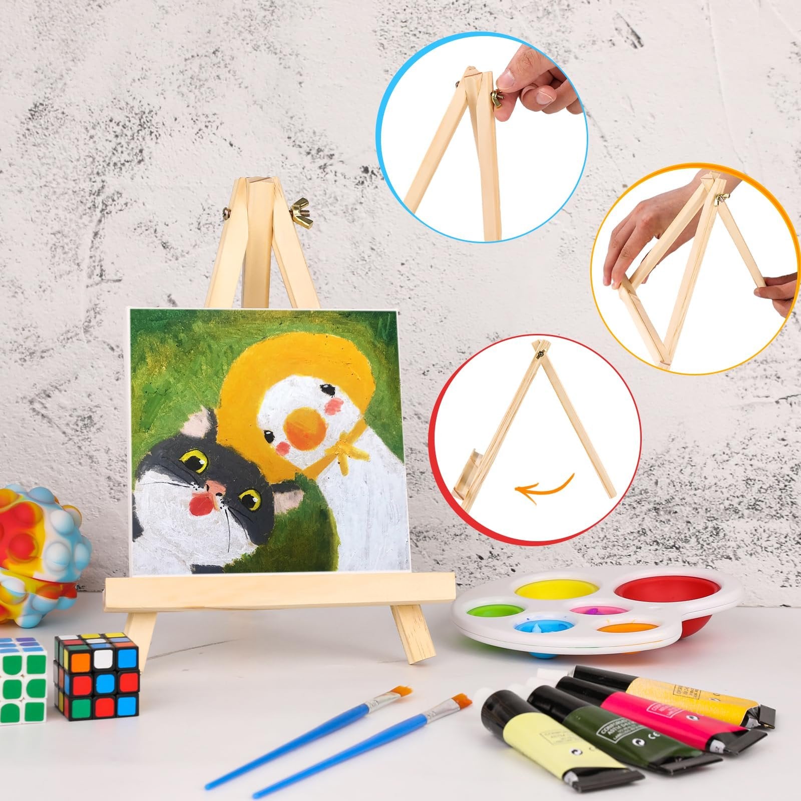 Wooden tabletop easel displaying a painting of a cat and duckling, with art supplies and fidget toys nearby.