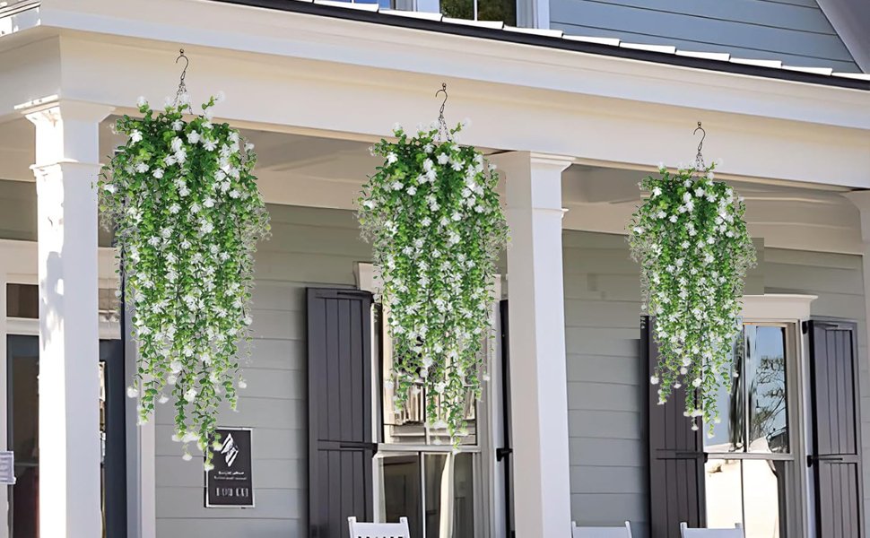 Three hanging baskets of artificial white flowers and green eucalyptus vines on a porch.