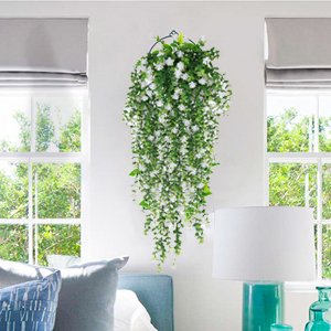 Artificial hanging white flowers with green eucalyptus vine garland displayed indoors on a white wall between two windows.